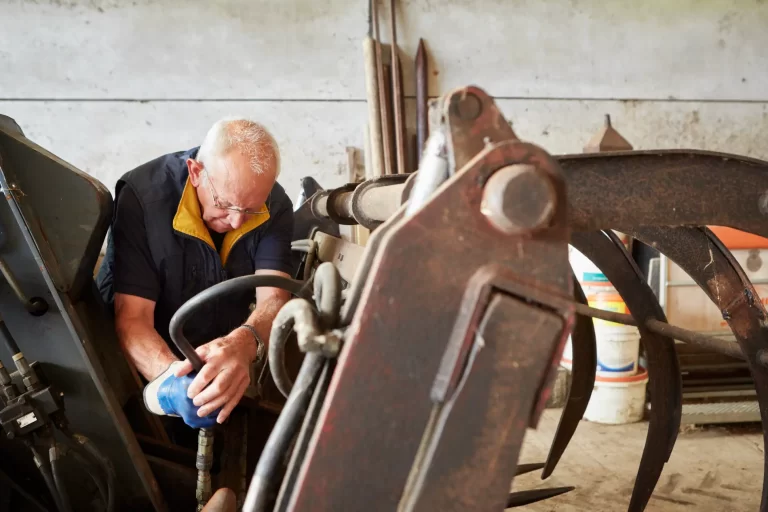 A man working with tools on farm machinery in a barn.