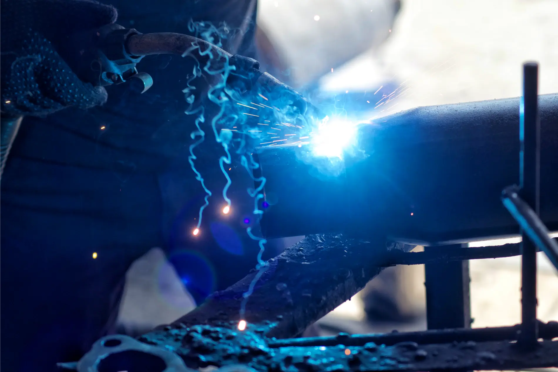 An unrecognizable industrial metalworker makes sparks fly and smoke as he welds steel