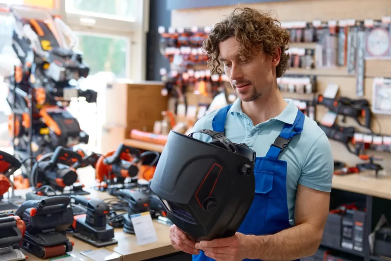 Workman in overalls choosing protective plastic welding mask at hardware store